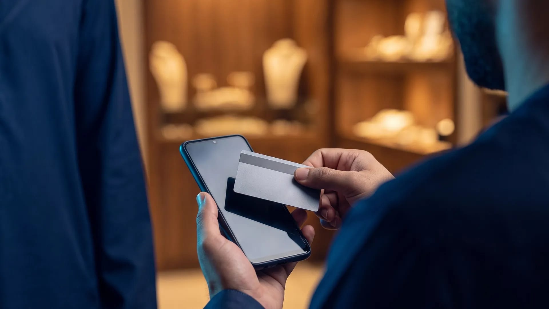 A shop worker holds an Android phone flat while a customer taps a contactless bank card against it to pay