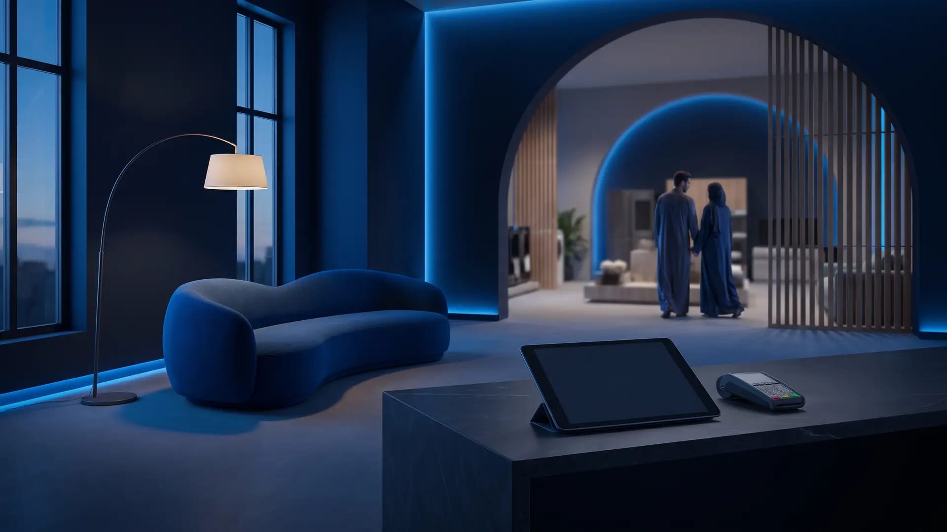 A modern Saudi furniture showroom at dusk with a sculptural sofa, a blank tablet on a stone sales desk and a couple browsing in the background